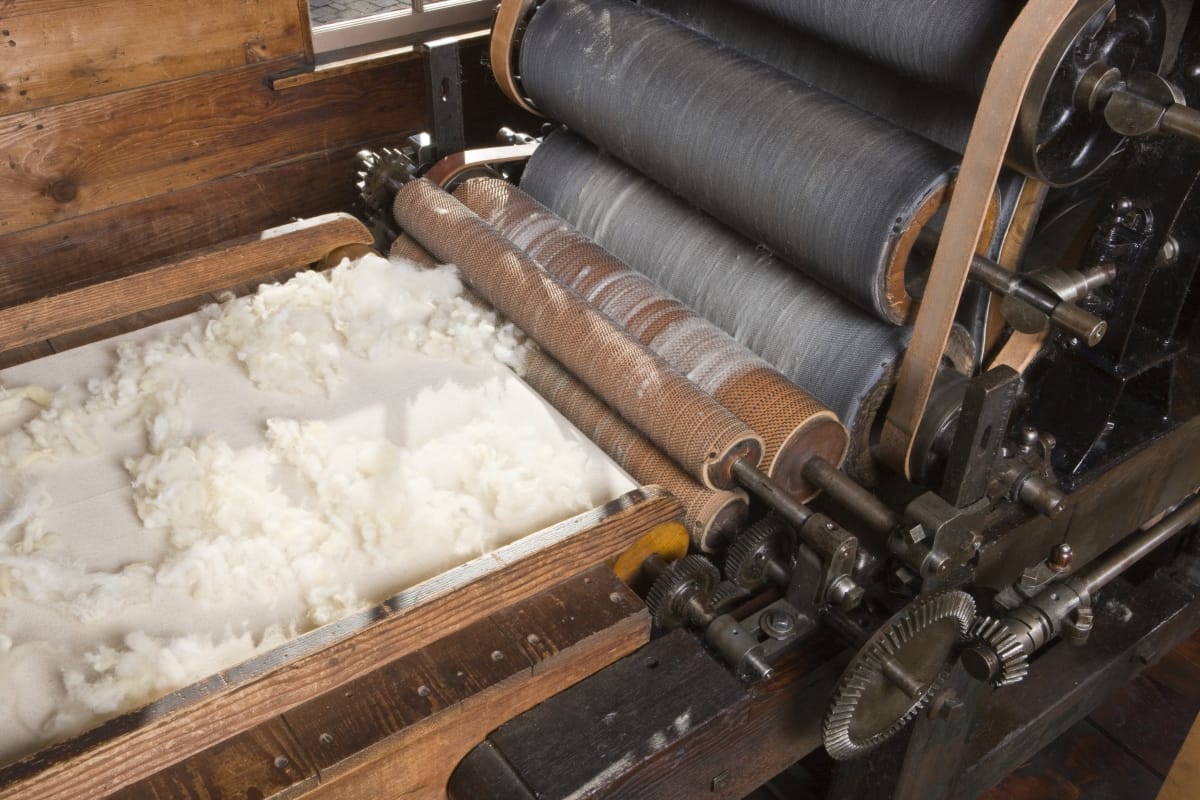 Conveyor belt with wool on it, headed for a machine with a series of large rollers