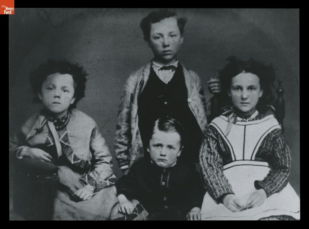 Black-and-white image of four children in old-fashioned clothing posing for camera