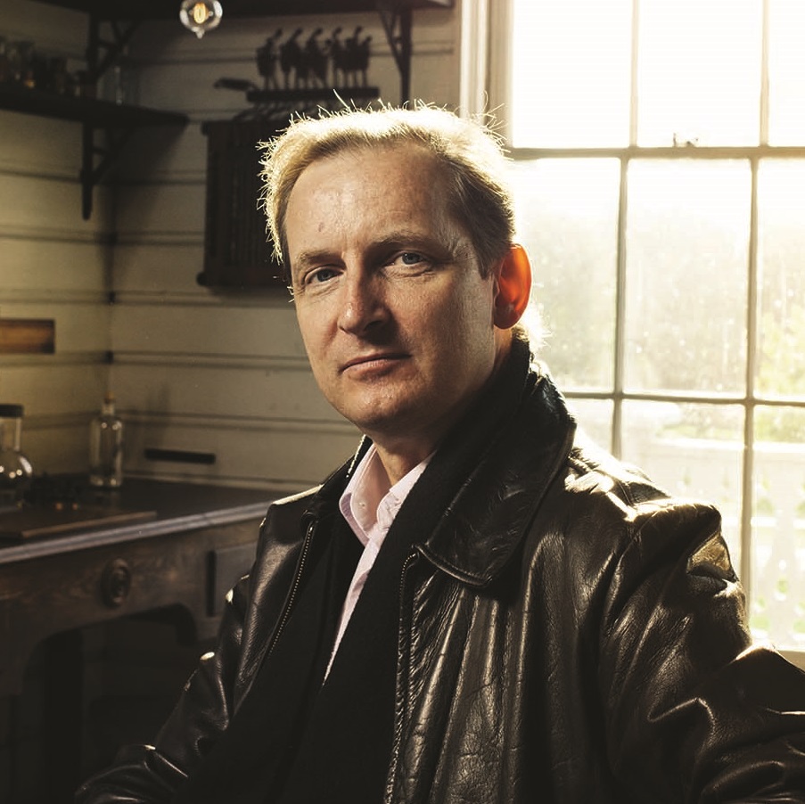 Portrait of man in black leather jacket sitting in workshop with window behind him