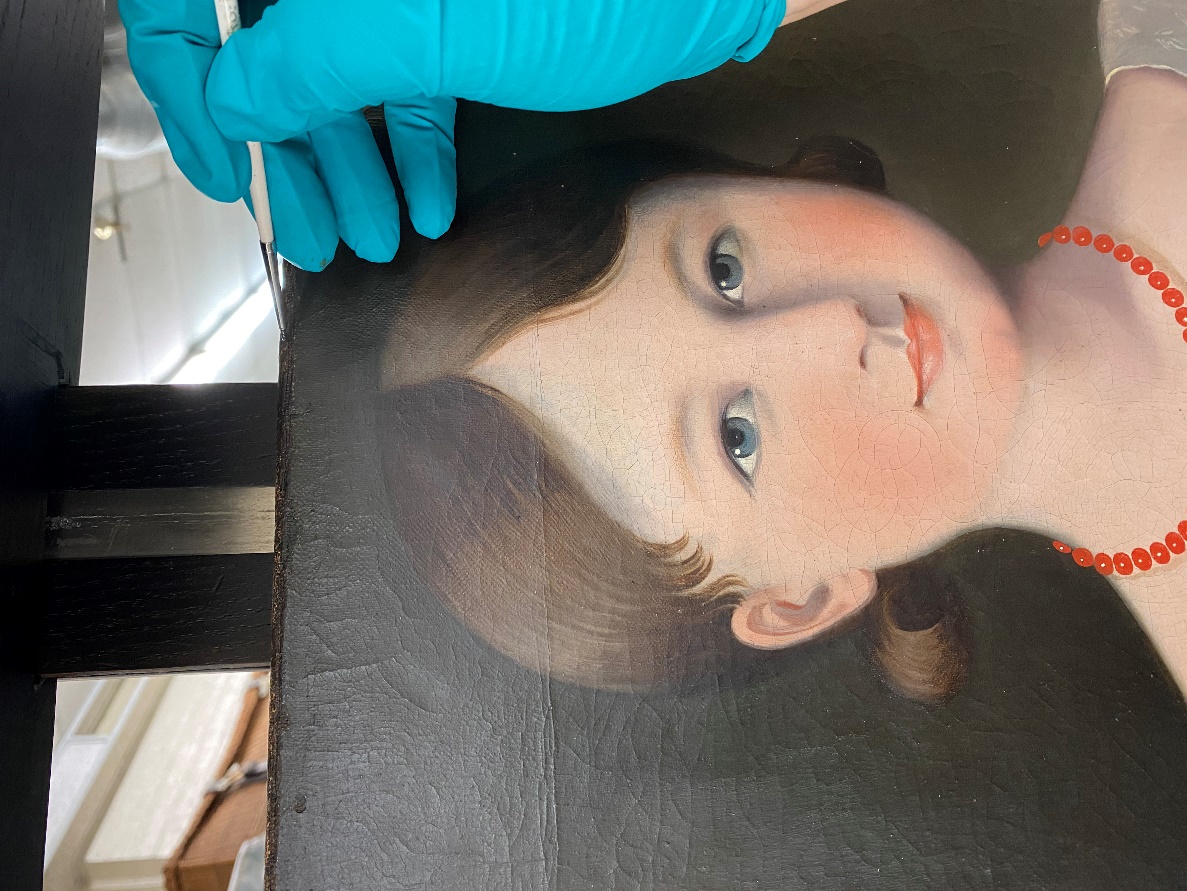 Blue-gloved hand holds a paintbrush at the top of a painting of a girl's head