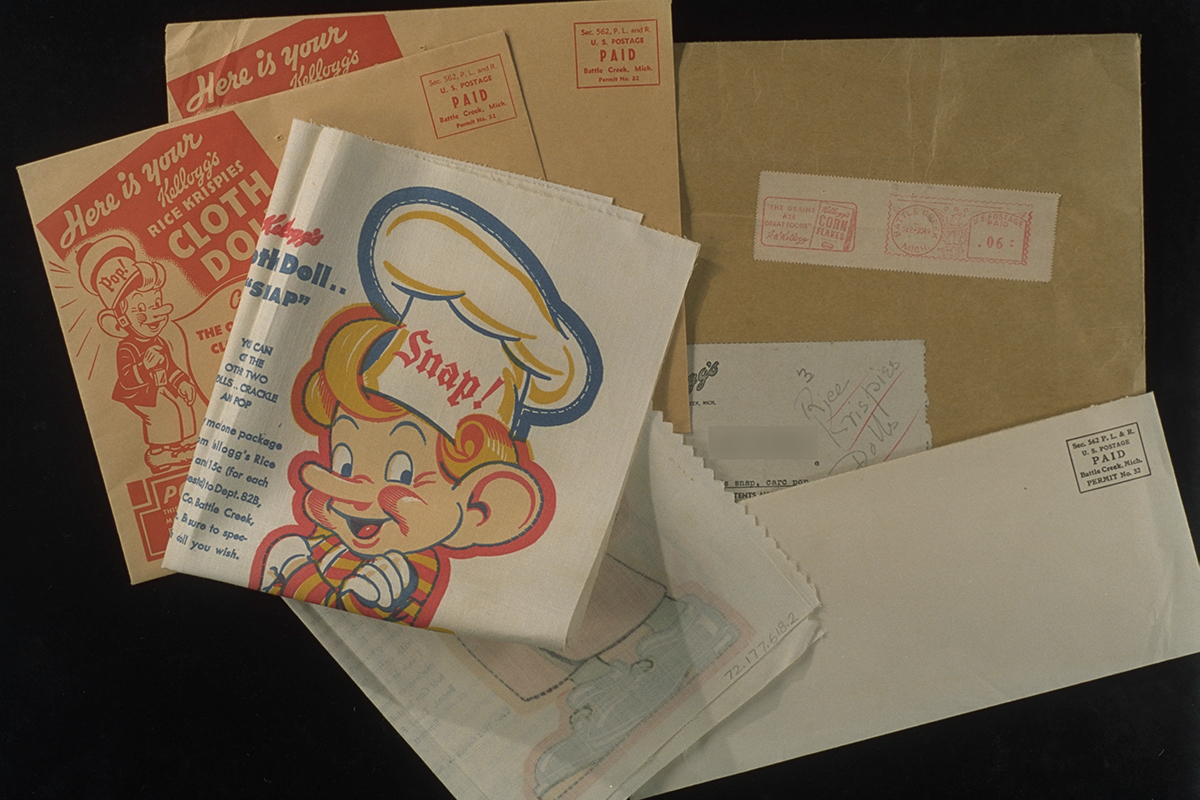 Several mailing envelopes and folded fabric showing elf head and torso with “Snap!” printed on chef’s hat 