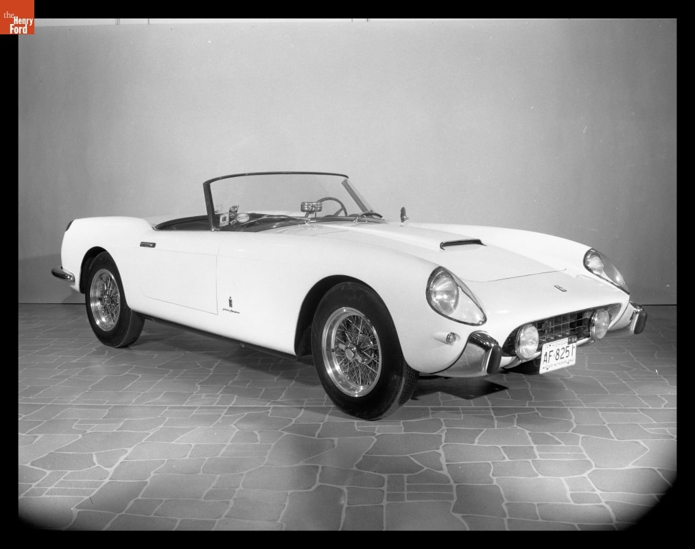 Black-and-white photo of sleek, low convertible with top down parked in a display indoors