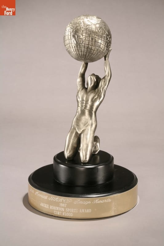 Silver trophy of kneeling man holding up a globe on black and silver base with text inscribed
