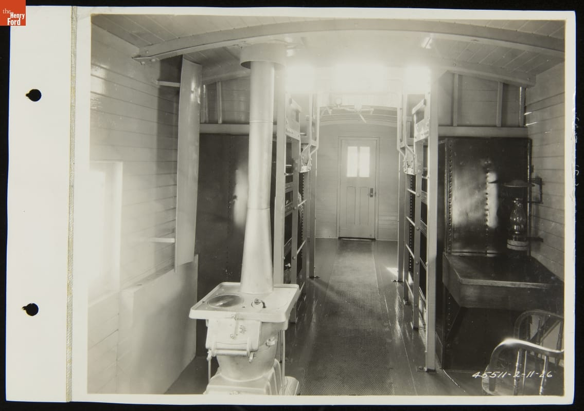 Interior of railcar, with stove, desk and chair, and shelving visible