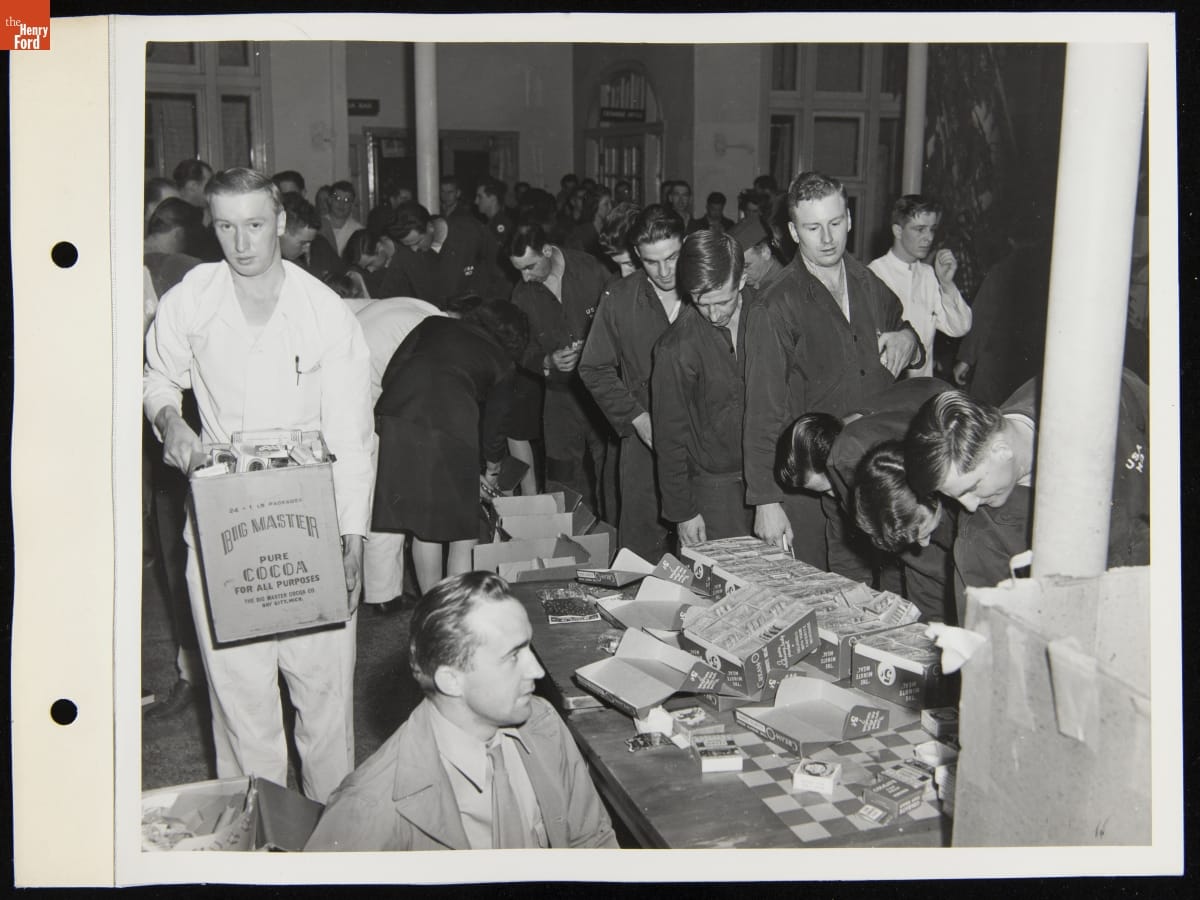 Room filled with people, some carrying boxes, and tables with boxes on them