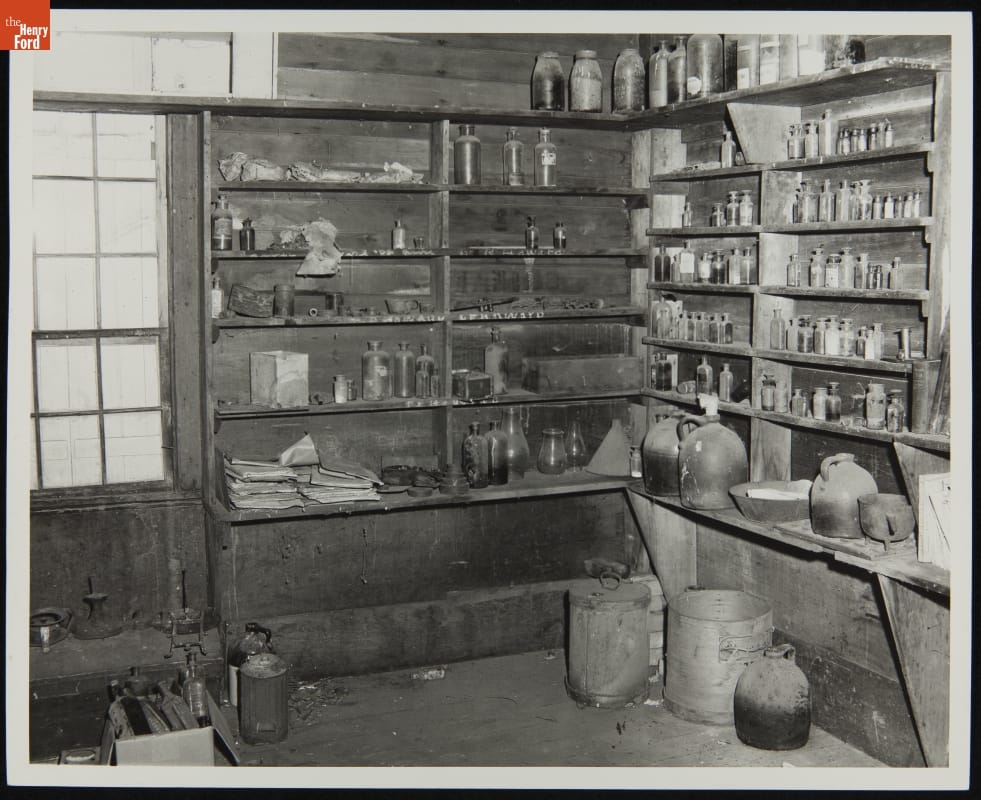 Interior of Dr. Howard's Office at Its Original Location, Tekonsha, Michigan, March 1956 Corner of simple wooden room with narrow shelves on the walls lined with bottles, jars, and papers