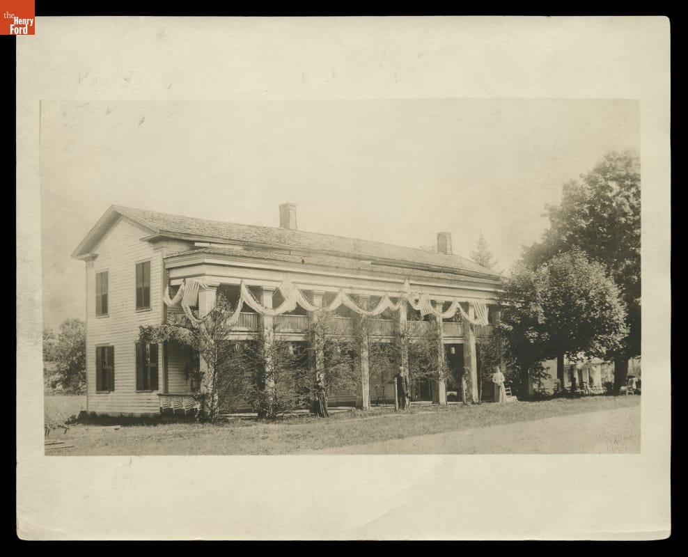 Eagle Tavern (Then Known as Smith's Hotel) at Its Original Site, Clinton, Michigan, circa 1890 Black-and-white photo of long, two-story building with pillars in front of a first-story porch and second-story balcony