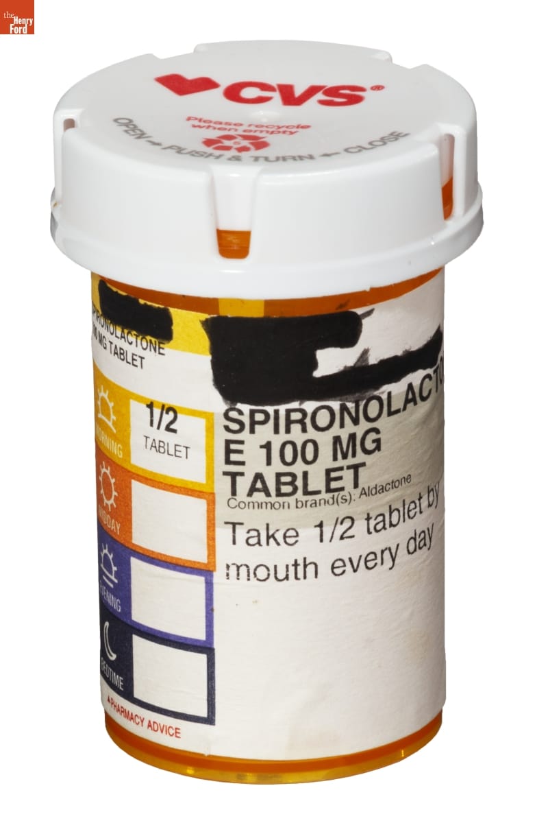Orange plastic prescription bottle with white lid and white label containing text (some of which is blacked out)