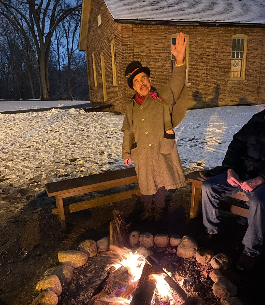 Anthony Lucas in “The Night Before Christmas” Man in duster coat and top hat by a fire pit waves to the camera