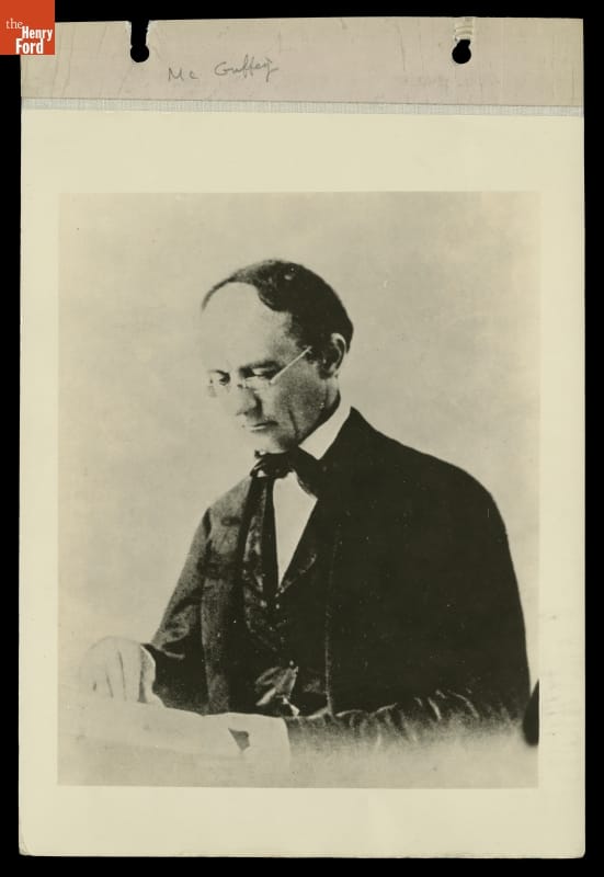 Photograph of man wearing glasses and a suit reading a book