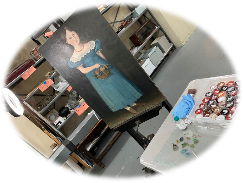 Oval image of painting of girl in blue dress on an easel; table nearby with palette and tubes of paints
