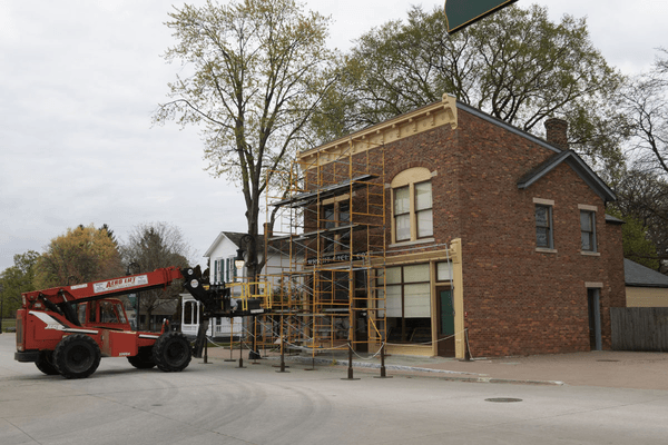 GIF cycling through several images of a forklift lifting a sign onto a building roof