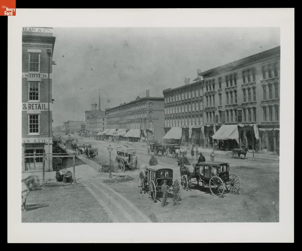 Horse-Drawn Vehicles on a Commercial Street in Detroit, Michigan, circa 1875 City street scene with buildings, horse-drawn carriages, and pedestrians