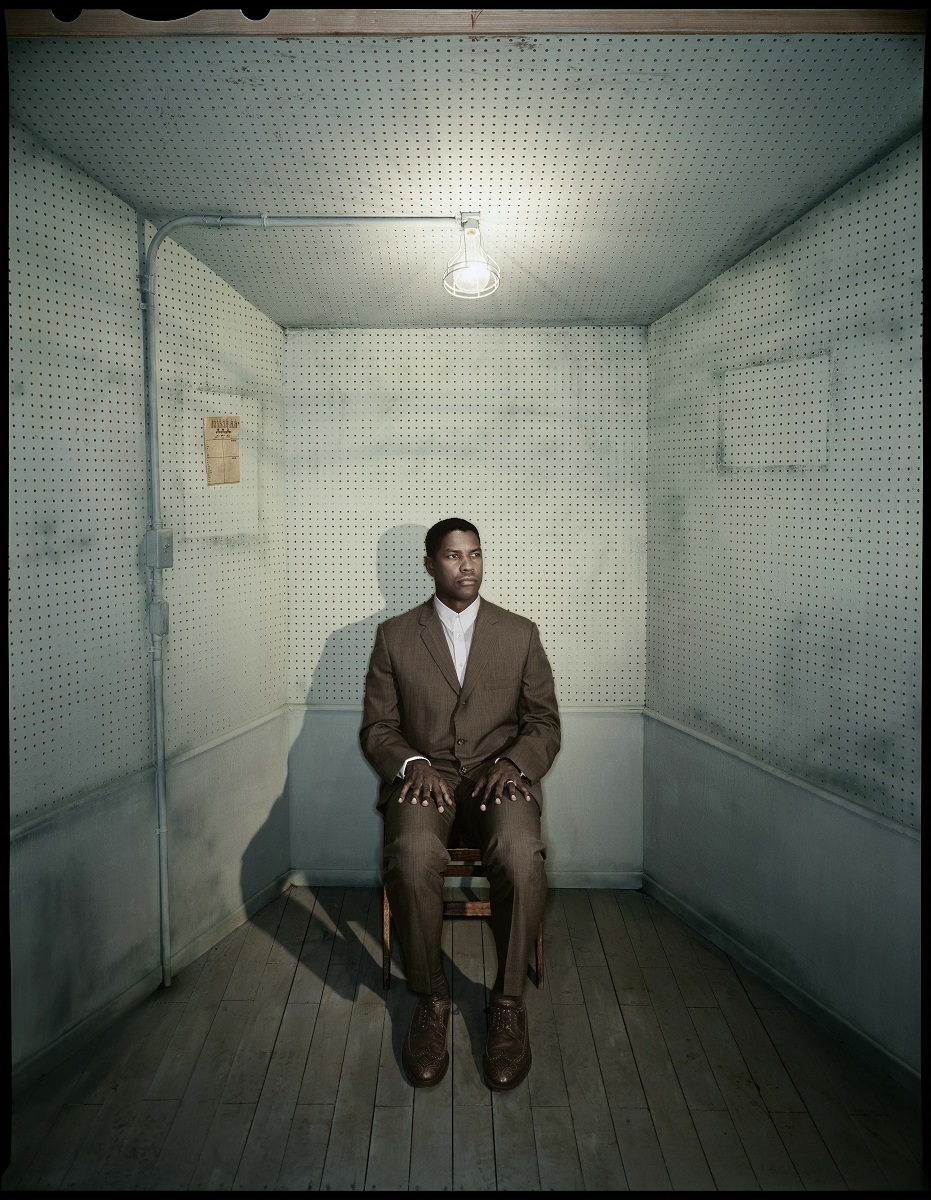 Man in suit sits with hands on thighs in room with skewed perspective