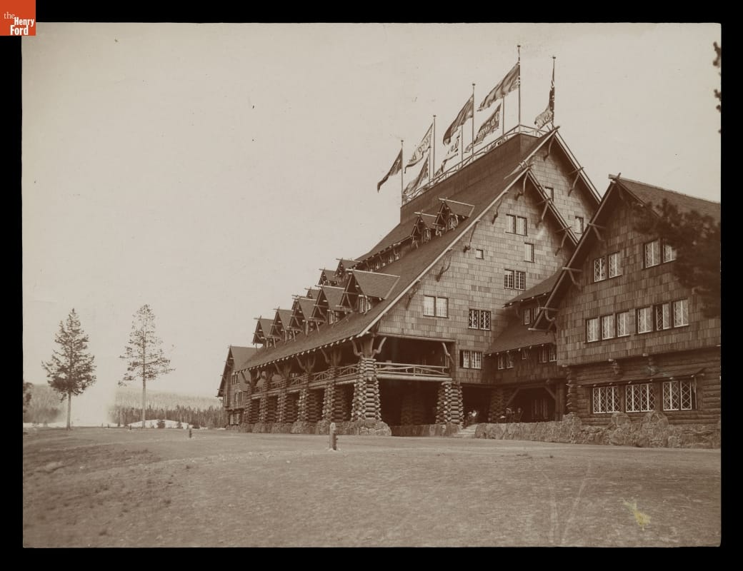 Black-and-white image of rustic building with steep roof, many gables, and flags at the top of the roofline