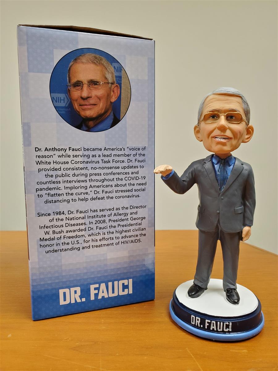 Large-headed figurine of man in gray suit with glasses, next to box containing photo of man's head and text