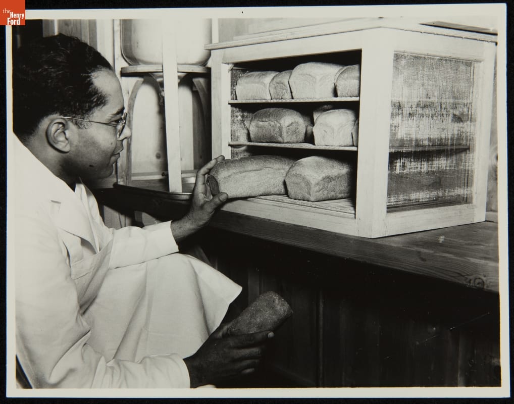 Paul Foster and Food Research in Henry Ford’s Laboratories, 1930-1942 Man kneels in front of cabinet full of loaves of bread to pull a loaf out