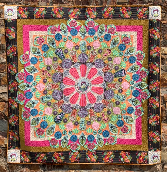 Multicolored quilt with pink flower in the center of concentric design