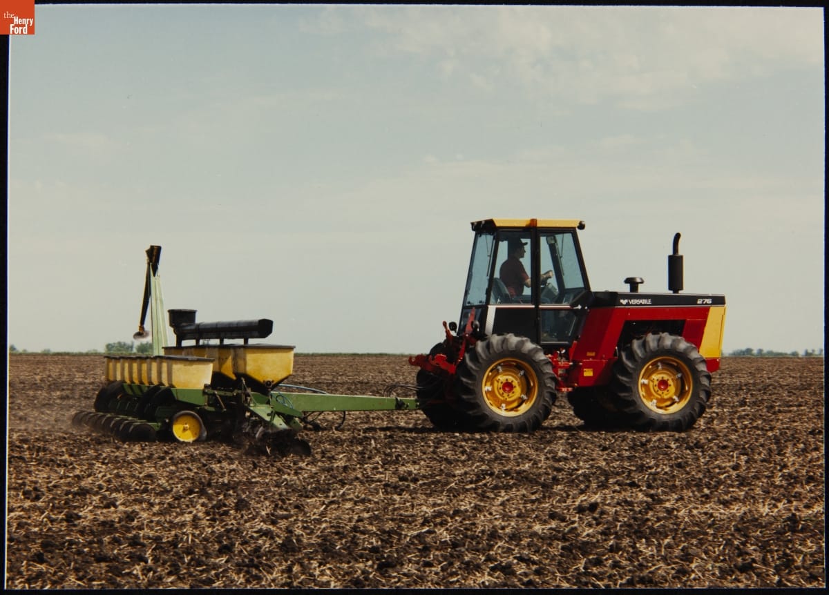 Versatile #276 Tractor Pulling a Deere Low-Till Planter, 1989 Small red tractor with enclosed cab pulling a planter through a dirt field