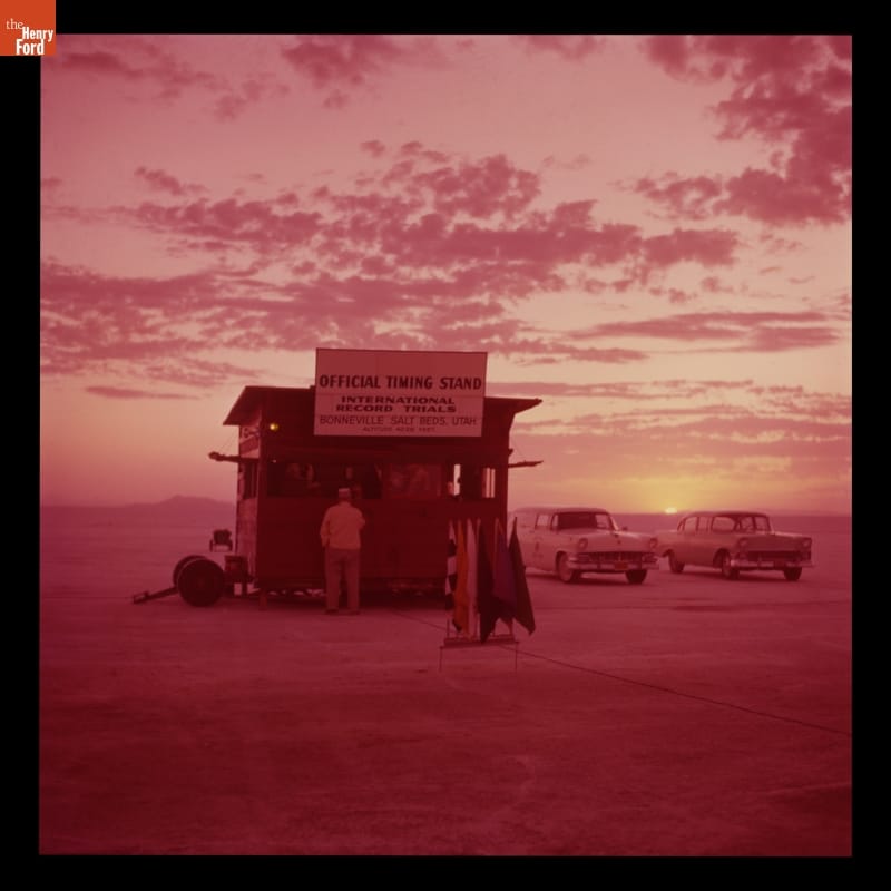 Official Timing Stand, Bonneville Salt Flats, Utah, 1956 Pink-tinted photo showing shack, people, cars in a large open expanse