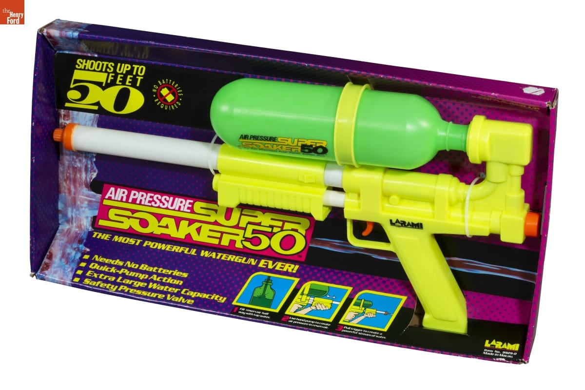 Purple and pink box containing large yellow and green water gun; also contains text