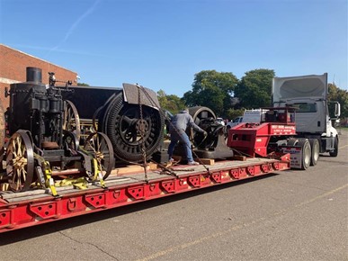Flatbed semi truck loaded with large machinery and person strapping it down