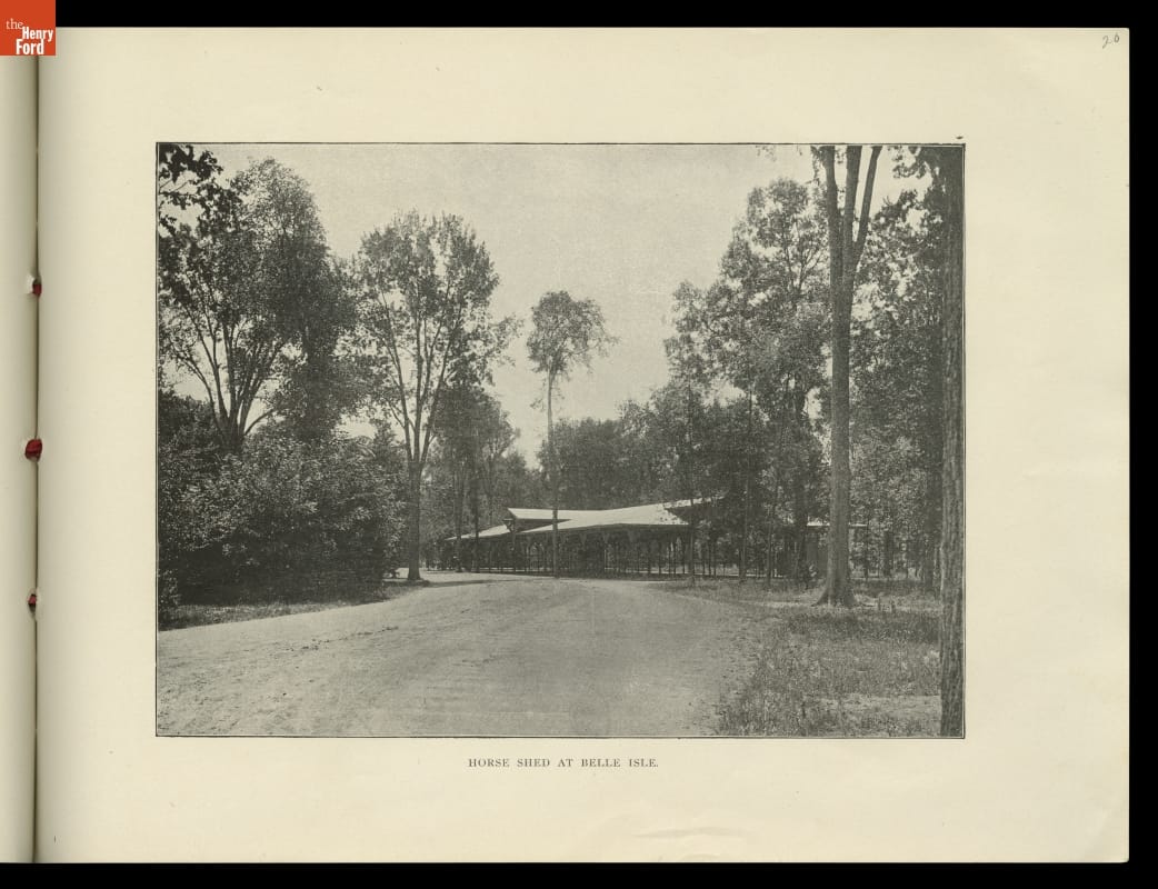 Page with black-and-white photograph of low open building among trees by dirt road; also contains text