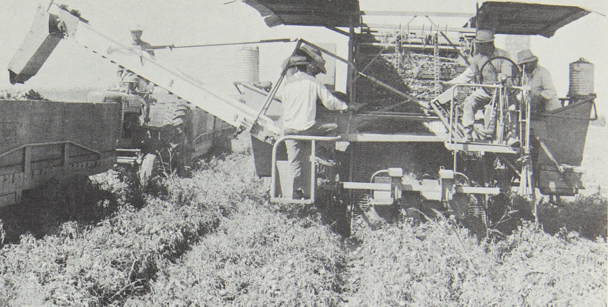 Large piece of mobile equipment in field with a number of people on it