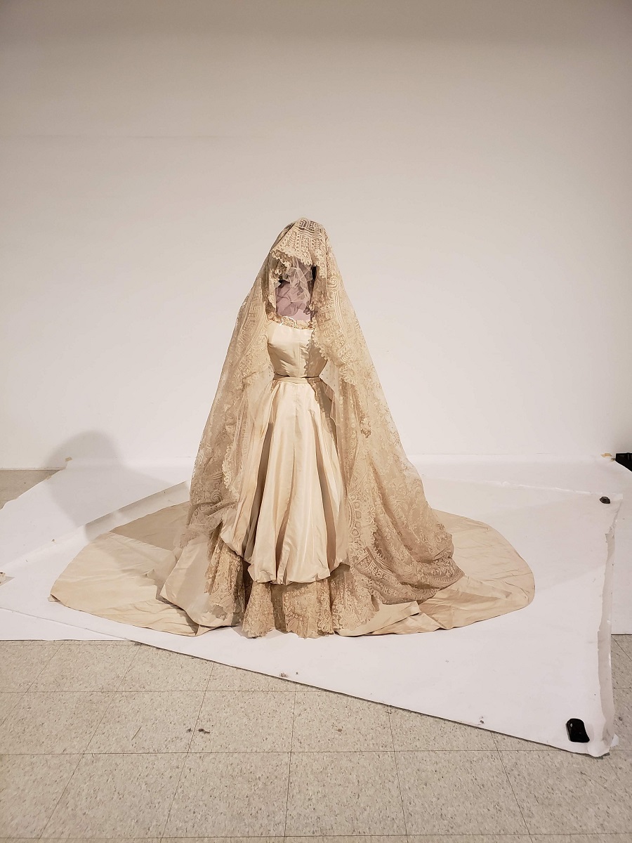 Wedding dress and elaborate veil/headdress on a mannequin standing on white paper