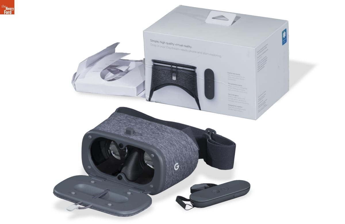 Gray fabric-covered goggles with closure, pictured with box and oval-shaped accessory