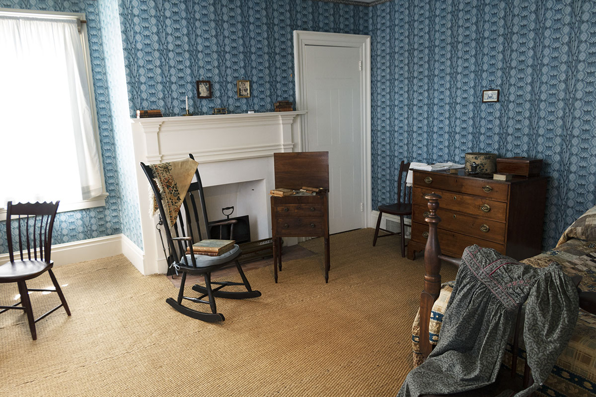 Noah Webster Home / bedroom Room with patterned blue wallpaper containing fireplace, bed, chest of drawers, chairs