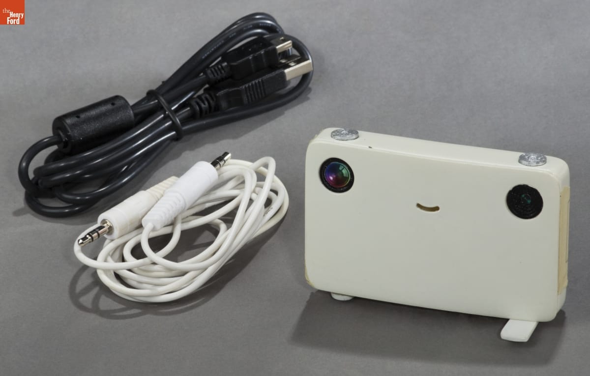 White rectangular device with a smiley face and two cords, one white and one black