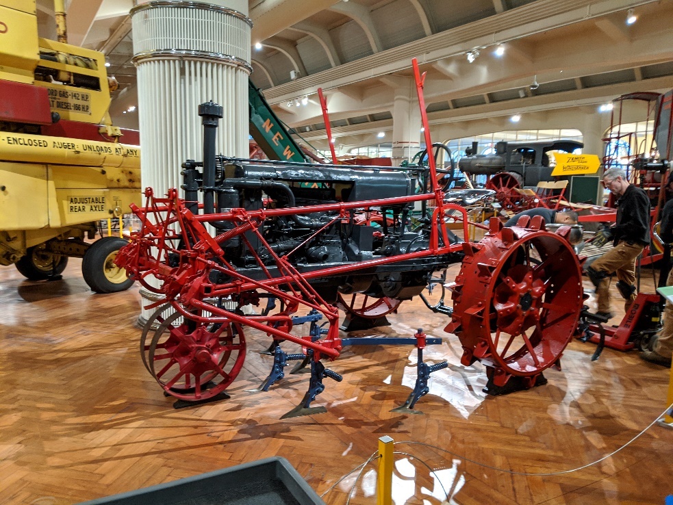 Tractor on wood floor in exhibit, surrounded by other equipment