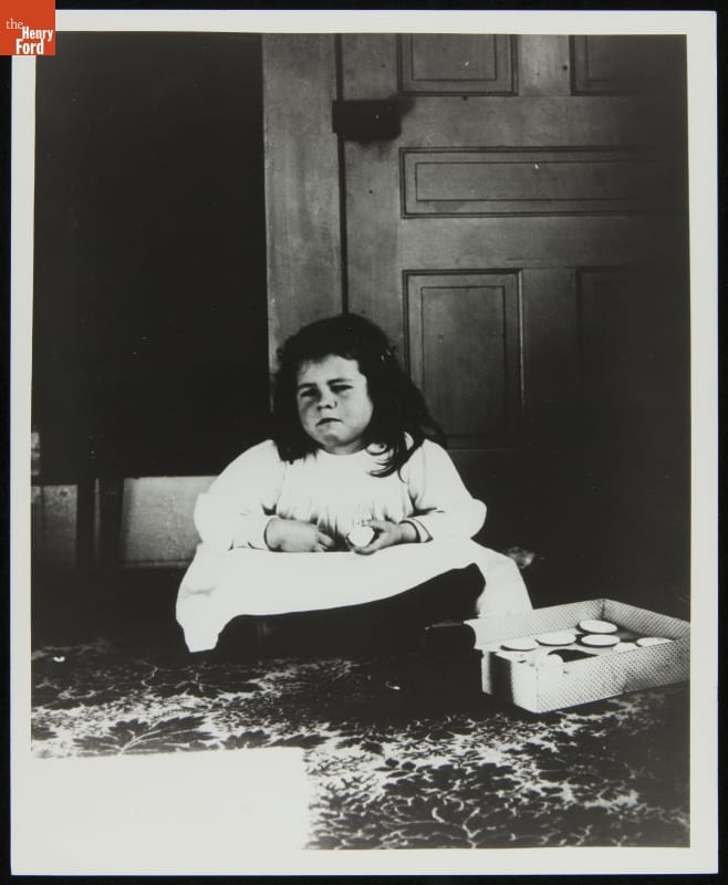 Girl in white dress sitting cross-legged with somewhat grumpy expression on her face