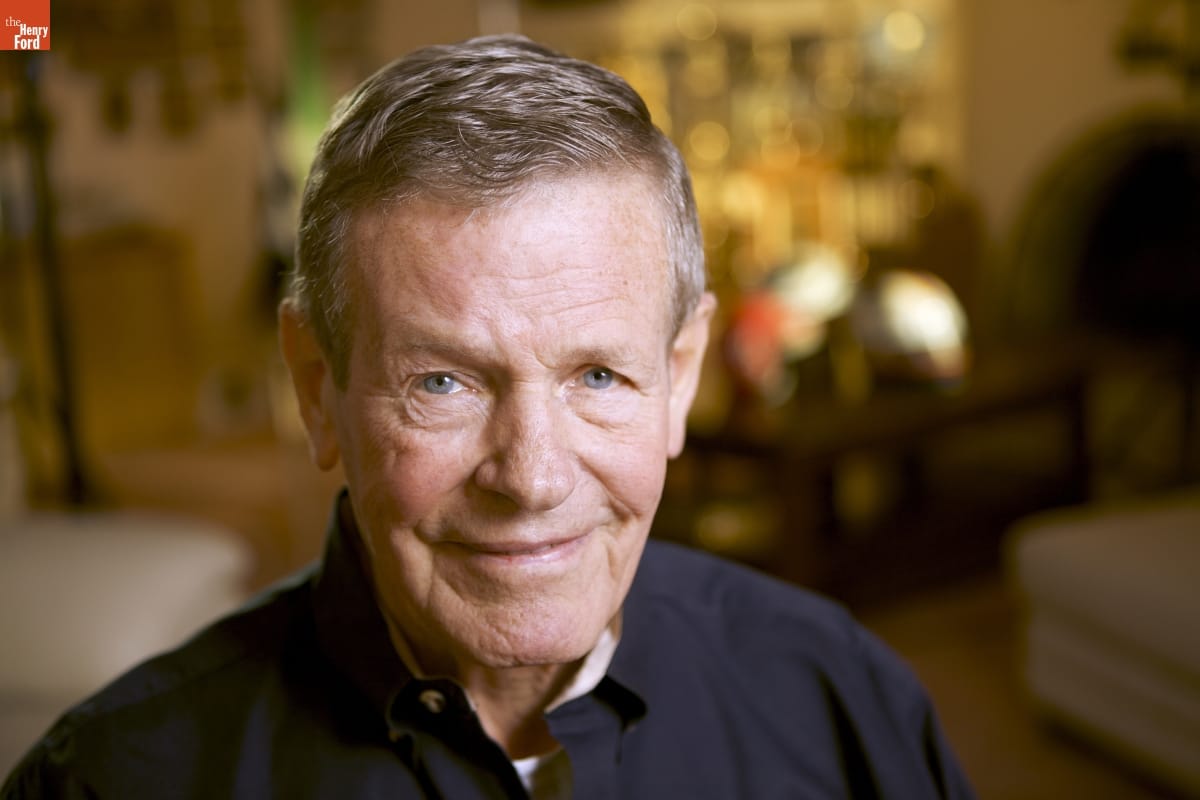 Close-up of man's head and shoulders, wearing black shirt and smiling at camera