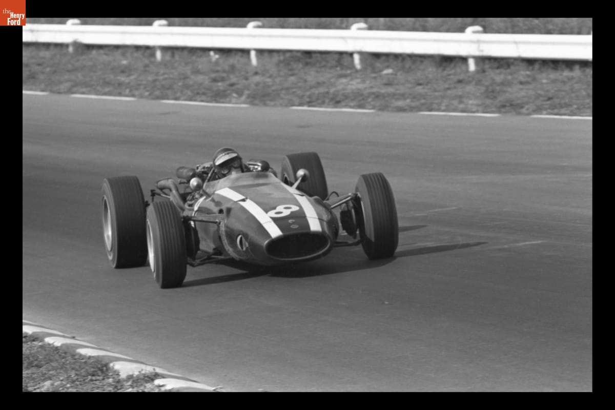 Race car with stripes and diagonal number 8 on hood, and person wearing helmet and goggles inside