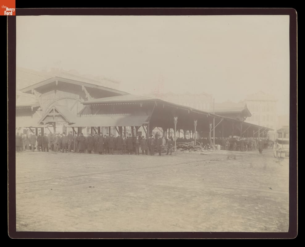 Large, low open building with many people gathered inside and near it