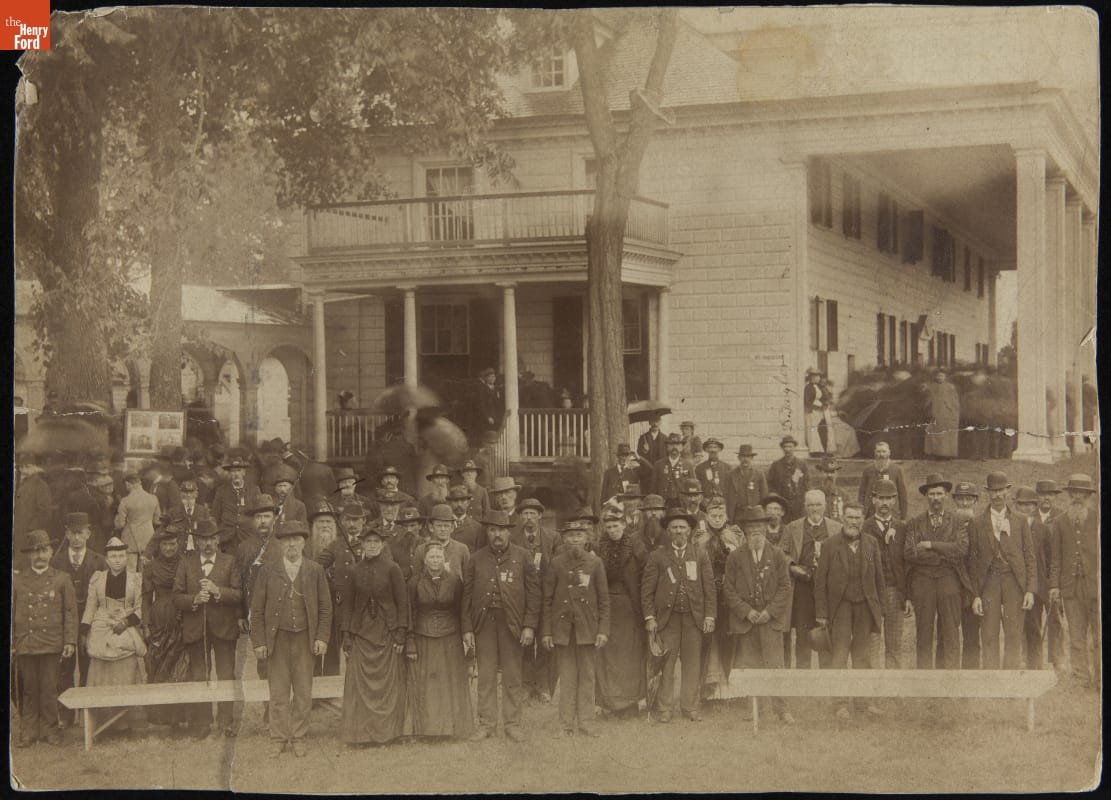 Large group of men and women posed in front of a large wooden building
