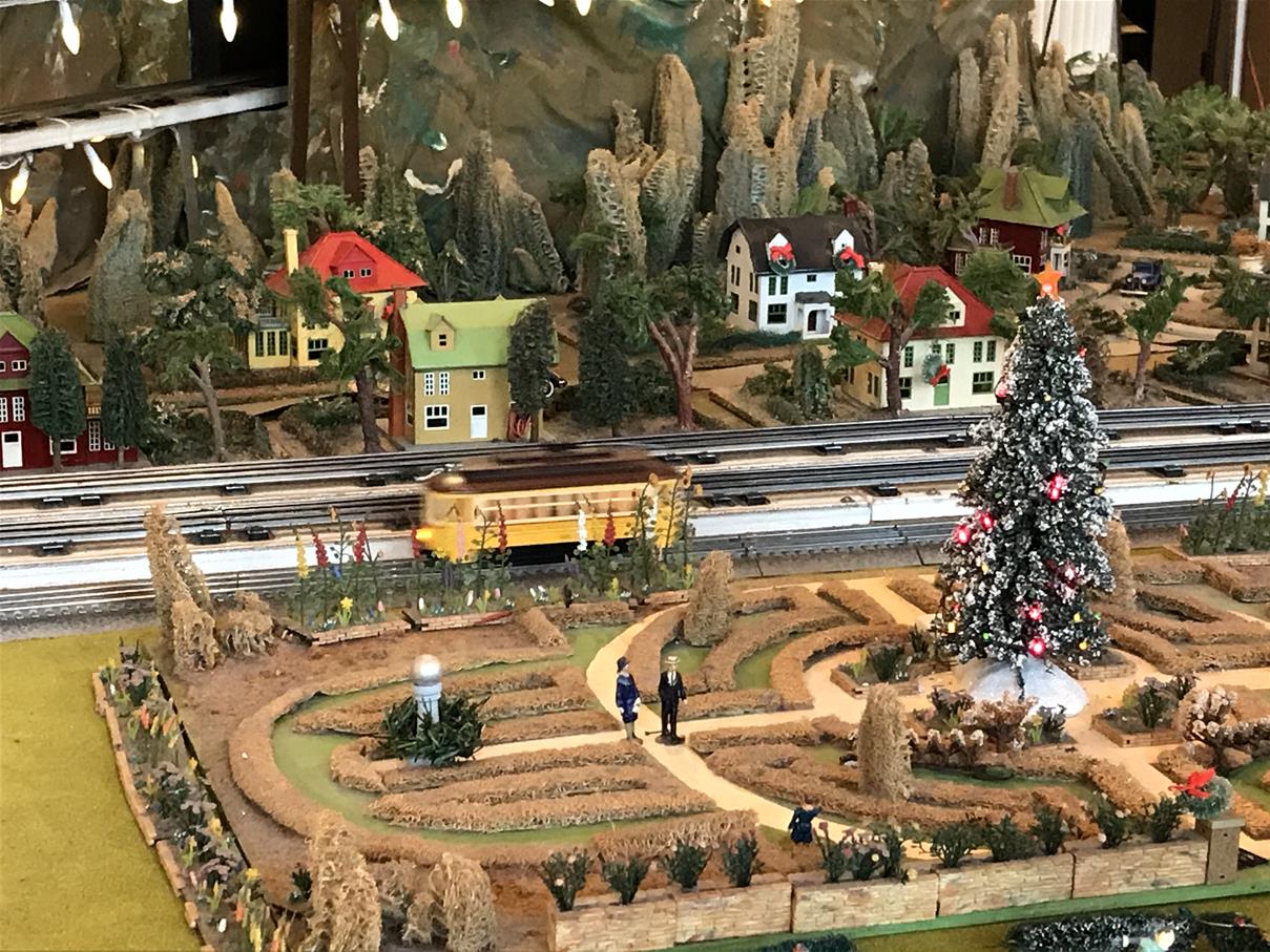 Model train layout with train tracks, train car, greenery, and houses, with Christmas decorations